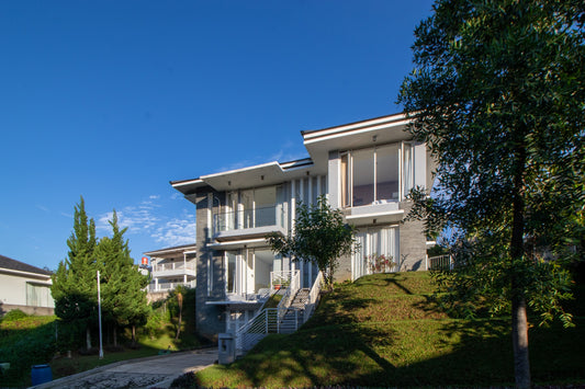 Sebuah vila bertingkat dengan eksterior putih ini memiliki 4 kamar tidur, terletak di daerah pegunungan tepatnya di Dago Bandung, dengan pepohonan dan tanaman rumput hijau di bagian depan dan belakang villa menambah sejuk suasana.