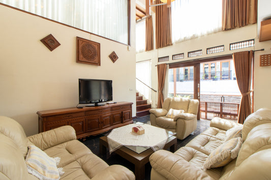 Villa dengan ruang tamu yang diisi sofa berukuran besar dan nyaman dengan hiasan bantal kecil dan meja di tengahnya, dilengkapi dengan smart tv yang menyajikan hiburan untuk kamu dan keluarga saat berkumpul di ruang keluarga.