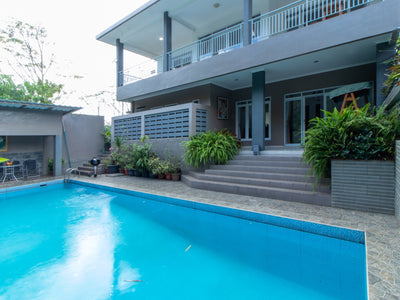 Villa dengan kolam renang pribadi yang terletak di bandung, menampilkan desain modern dengan balkon dan dikelilingi oleh tanaman hijau subur.