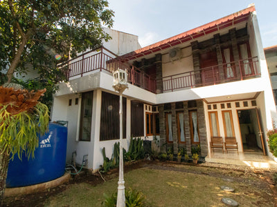 Tampak samping Villa Dago35 dua lantai dengan balkon dan taman asri, dikelilingi pepohonan rindang