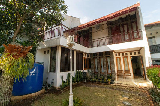 Tampak samping Villa Dago35 dua lantai dengan balkon dan taman asri, dikelilingi pepohonan rindang