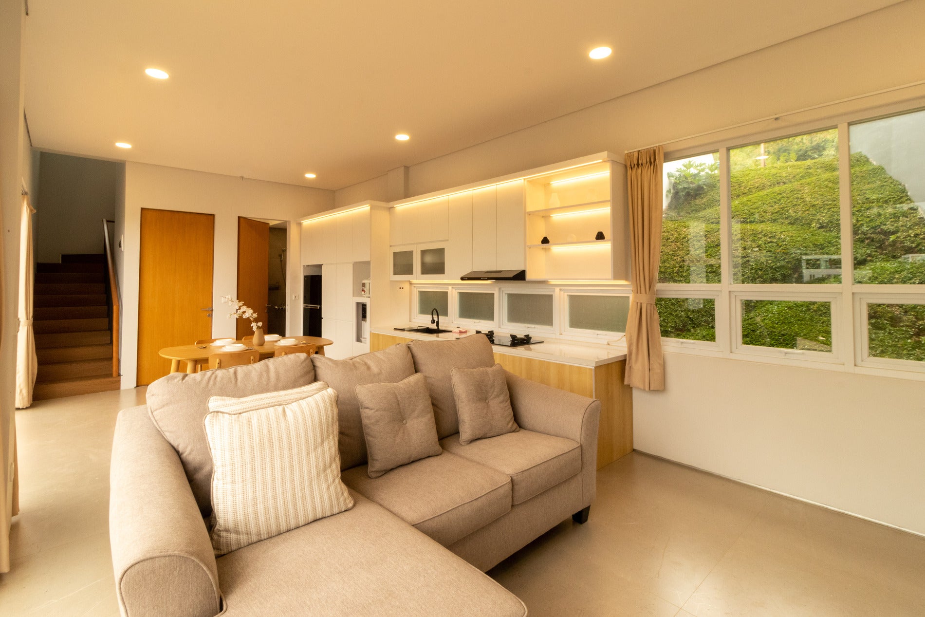 Nikmati momen kebersamaan saat di villa ruang keluarga modern, yang didesain tanpa sekat. Didominasi oleh sofa berwarna beige yang elegan dan empuk, area ini menjadi tempat ternyaman untuk bersantai. Adanya jendela besar di sekeliling ruangan memastikan sirkulasi udara pegunungan yang segar dan cahaya matahari masuk dengan sempurna, memberikan kesan ruang yang sangat luas. Tersedia area dapur modern yang terintegrasi, memudahkan kamu menyiapkan kudapan sambil tetap berbincang dengan keluarga.