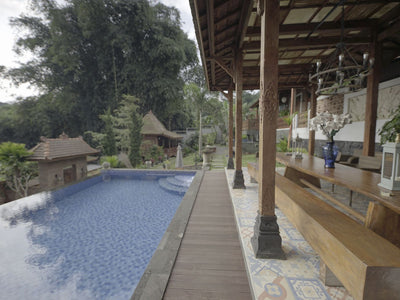 Area tepi kolam renang luar ruangan yang mewah di villa lembang dengan dek kayu, kolam renang biru, dan pagar kayu yang menghadap ke lanskap hijau subur